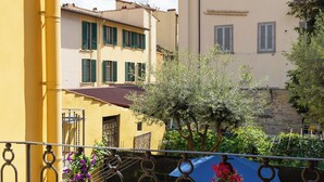 A balcony with a wrought iron railing, a yellow building, and a tree with pink flowers.