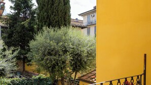 A balcony with a yellow wall, a metal railing, and hanging flowers.