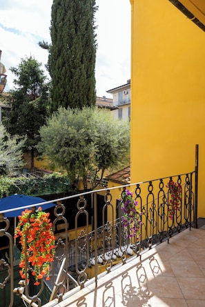 A balcony with a yellow wall, a metal railing, and hanging flowers.