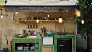 Eine Küchenzeile mit grüner Fliesenrückwand, einem schwarzen Kühlschrank sowie verschiedenen Küchengeräten und Utensilien.
