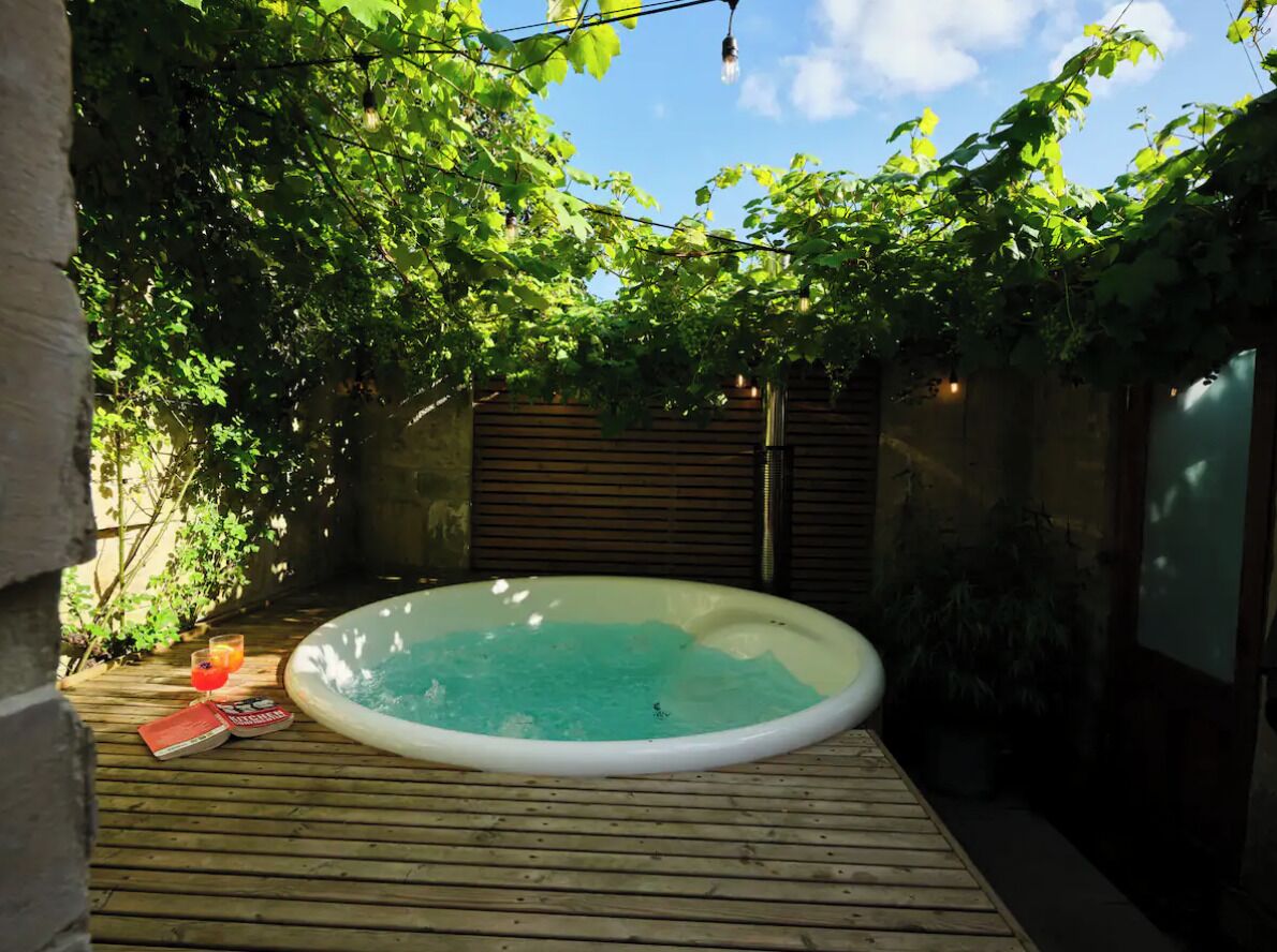 Een hottub omringd door een houten terras, met een bakstenen muur en begroeiing op de achtergrond.