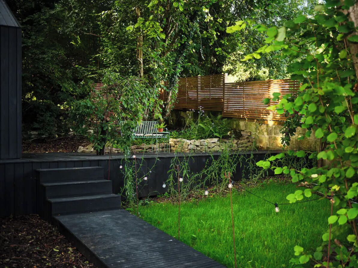 Un jardin avec un banc en bois, un mur de pierre et un petit escalier menant à une structure sombre.