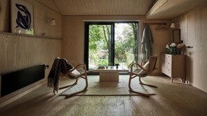 Ein Zimmer mit großem Fenster, Holzboden, einer Couch, einem Tisch und einem Schrank.