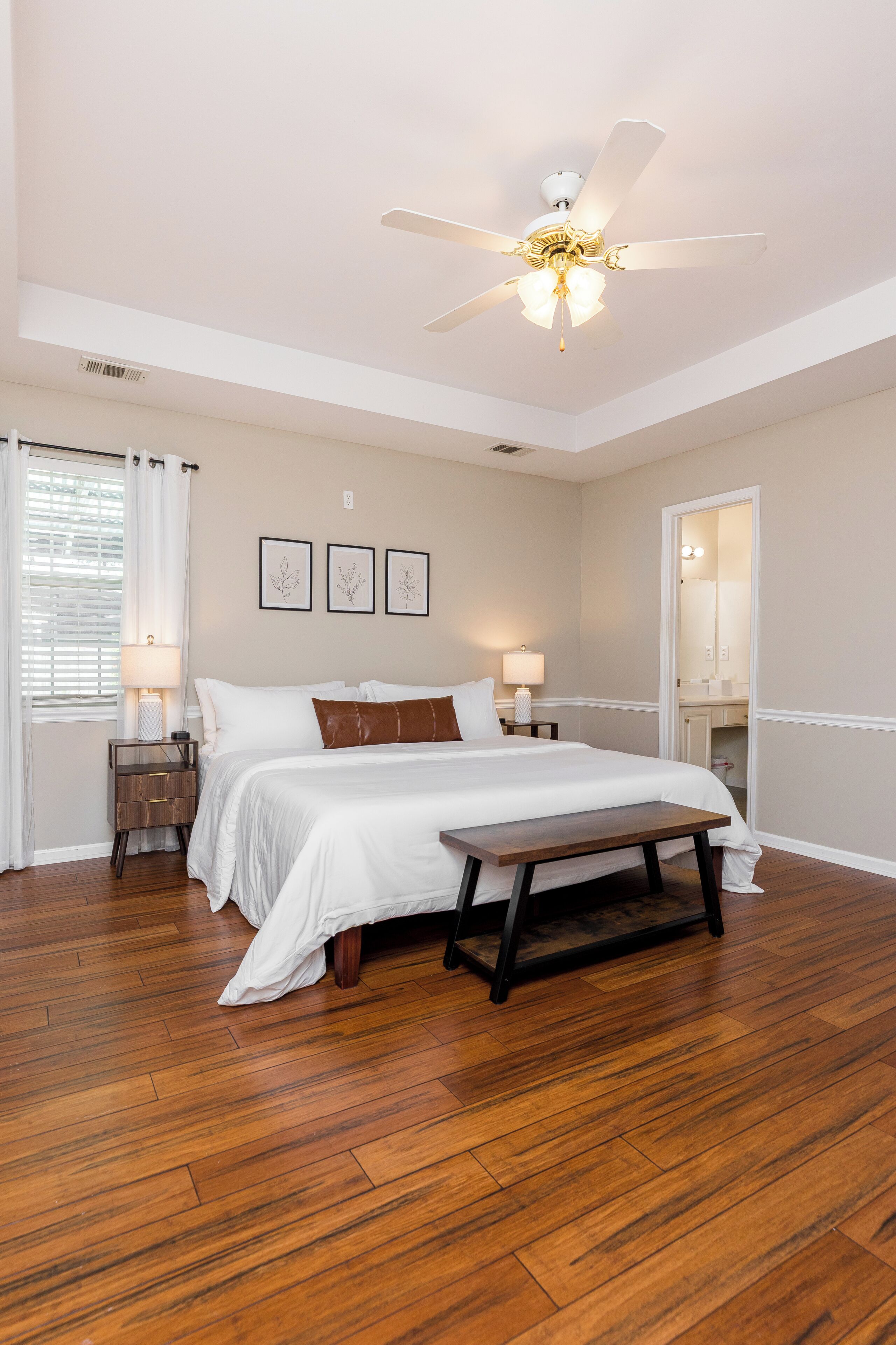 A bedroom with a bed, bedside tables, a ceiling fan, and a wooden bench.