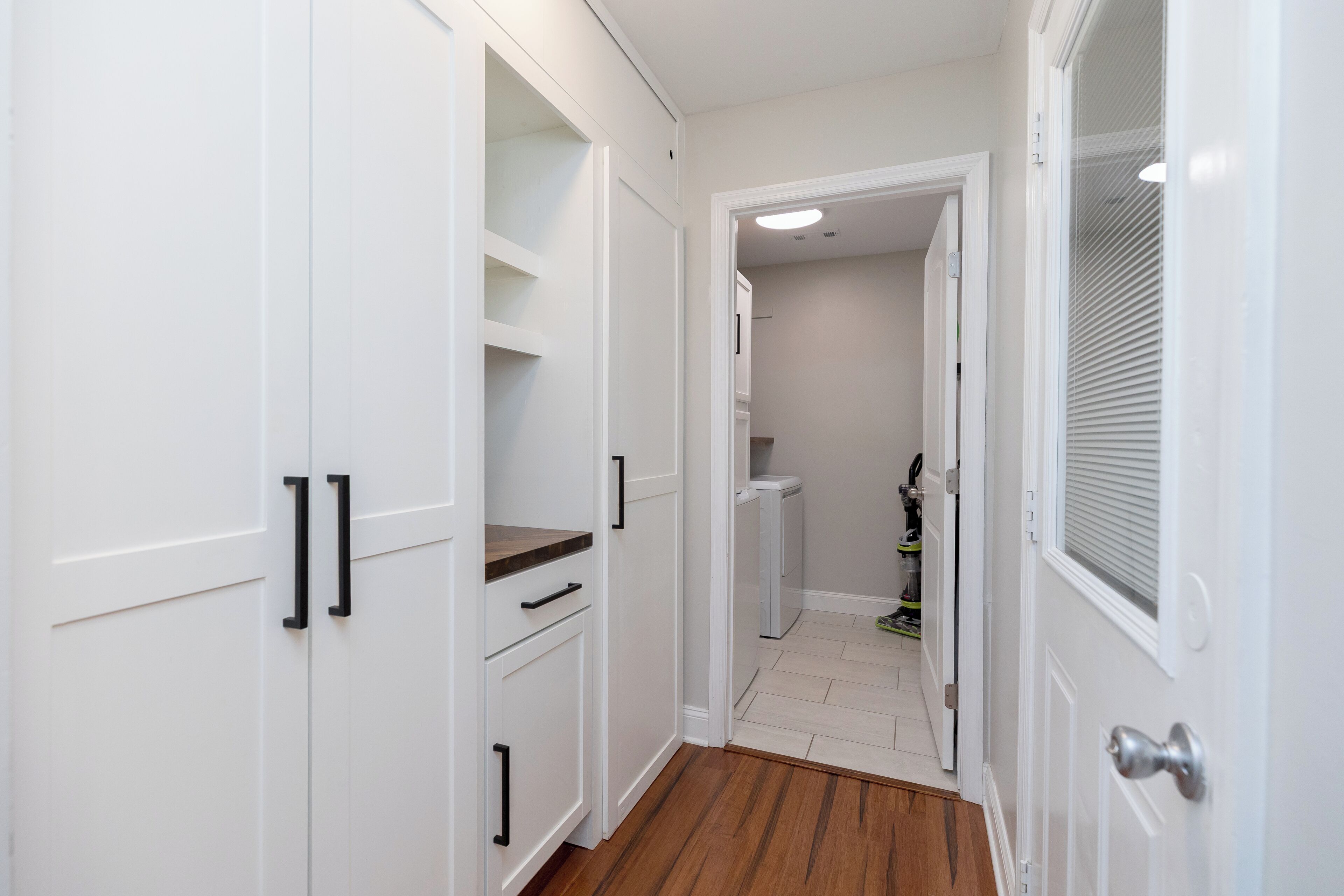 Passadís estret amb armaris blancs, un paviment de fusta i una porta que dona a una habitació amb radiador.