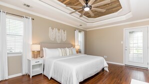 A bedroom with a wooden ceiling, a bed with white bedding, a nightstand with a lamp, and a door with a glass panel. - Pool + Fenced Yard | 4BR Family Home | Close to 96 (Warner Robins)