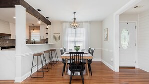 A dining area with a wooden table, black chairs, a chandelier, and a kitchen in the background. - Pool + Fenced Yard | 4BR Family Home | Close to 96 (Warner Robins)