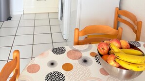A compact kitchen with a washing machine, a microwave, and a refrigerator. There is a table with a fruit bowl and a chair. - St Cyprien, right on the water, beach or swimming pool (Saint-Cyprien)
