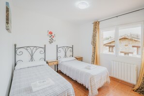 A room with two beds, a window with a view of buildings, a radiator, and a wall decoration. - Los Mirlos Country House – Nature Retreat with Garden and Social Lounge (Navaluenga)