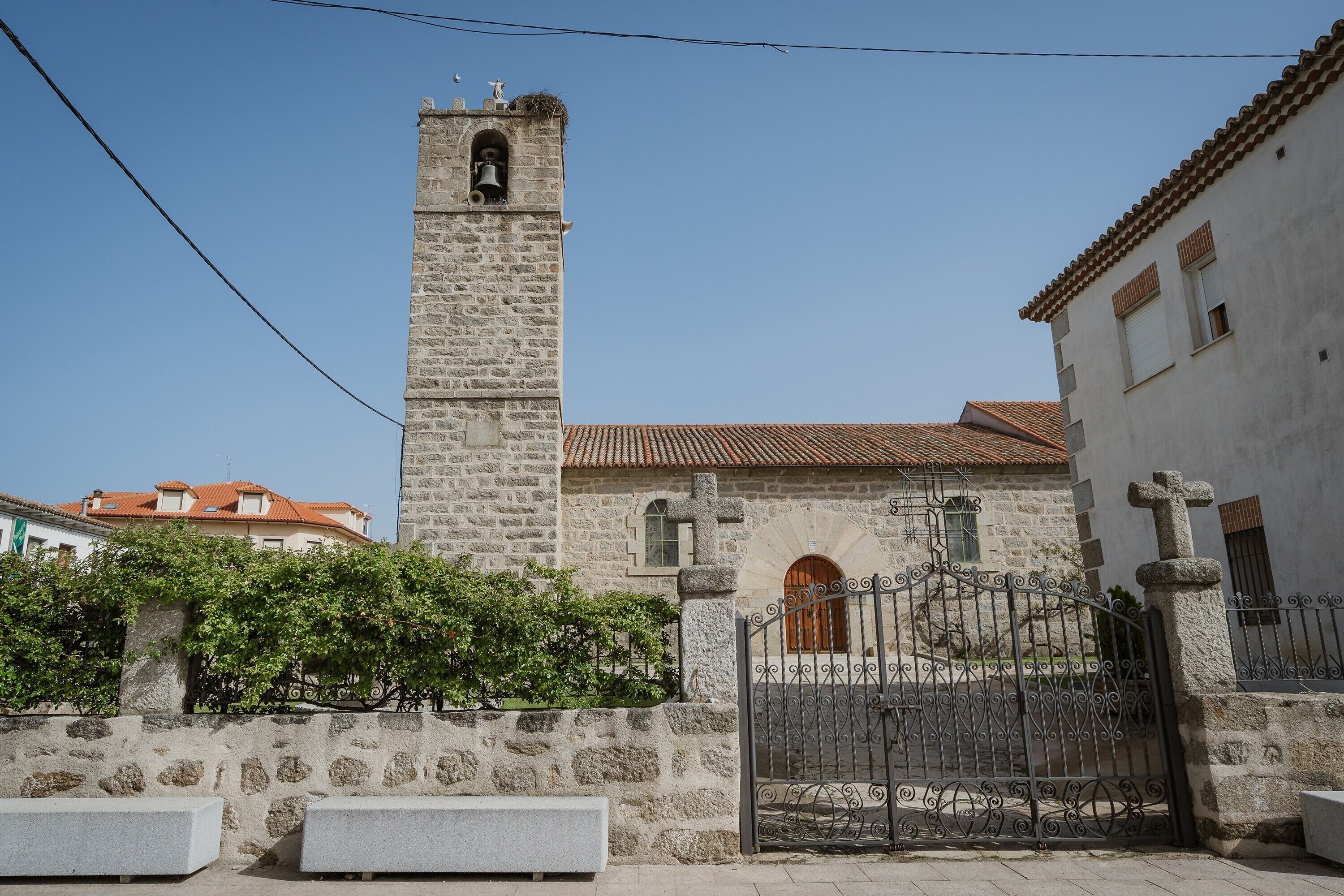 A stone church with a bell tower, a gated entrance, and a stone wall with benches.