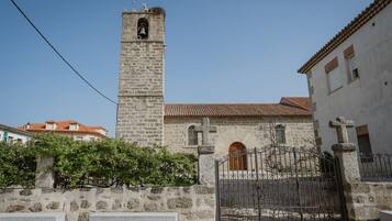 A stone church with a bell tower, a gated entrance, and a stone wall with benches.