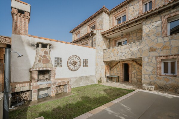 A courtyard with a stone fireplace, a circular window, and a stone wall. - Los Mirlos Country House – Nature Retreat with Garden and Social Lounge (Navaluenga)