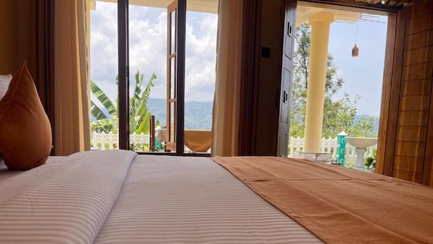 Ein Bett mit gestreifter Bettdecke und brauner Decke, ein Fenster mit Vorhängen und Blick auf einen weißen Zaun und Grünfläche draußen.