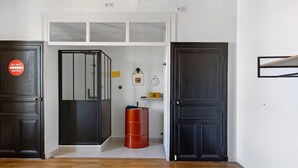Une pièce comprenant un lit, une armoire, une porte avec une pancarte indiquant « Défense d’entrer », un baril rouge et un mur blanc avec une étagère.