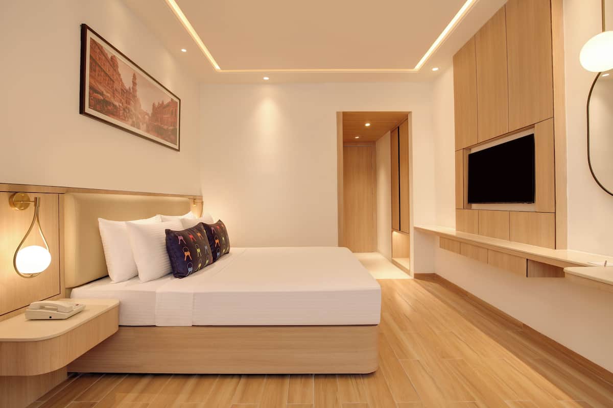 A modern hotel room with a large bed, a TV mounted on the wall, and a wooden floor.
