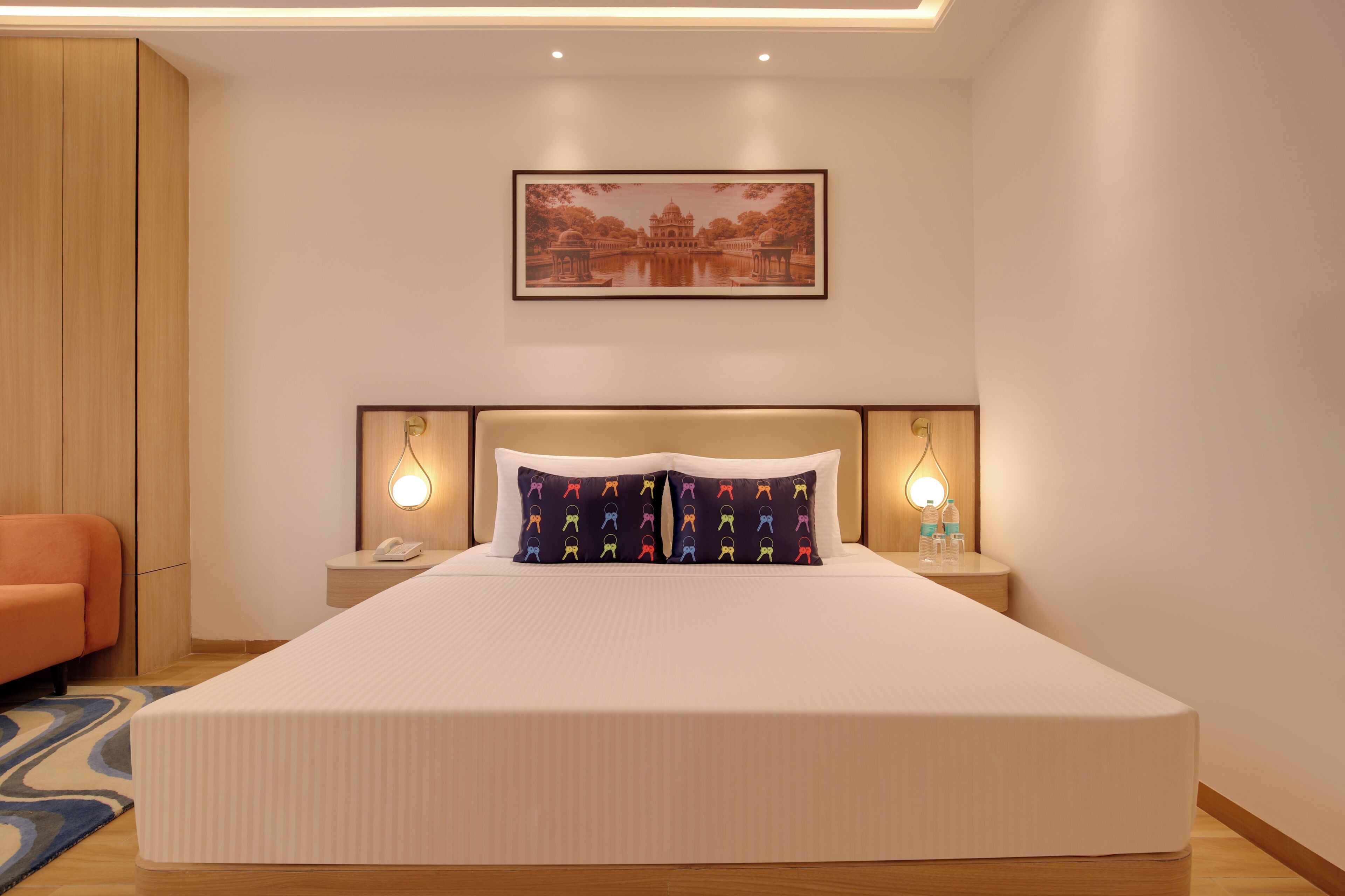 A hotel room with a large bed, two bedside tables, a nightstand, a chair, and a framed picture on the wall.