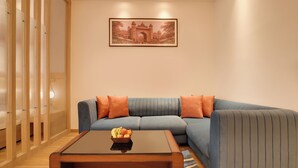 Un salon avec un canapé bleu, des coussins orange, une table basse sur laquelle on peut voir des fruits, et un tableau encadré accroché au mur.