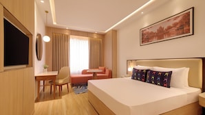 Une chambre d’hôtel avec un lit, un bureau, une chaise, un canapé, une télévision et un tableau au mur.