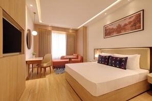 A hotel room with a bed, a desk, a chair, a sofa, a TV, and a painting on the wall. - Keys Select by Lemon Tree Hotel Amritsar (Amritsar)