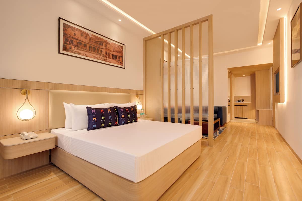 A modern hotel room with a large bed, bedside lamps, a wooden headboard, a framed picture on the wall, and a wooden floor.