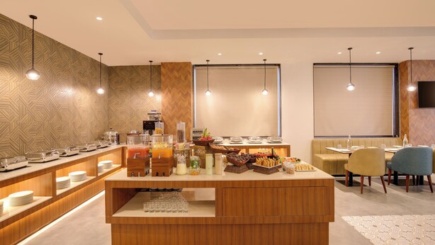 Un bar à petit-déjeuner moderne, proposant une variété d’aliments et de boissons, doté de meubles en bois et d’un éclairage suspendu.