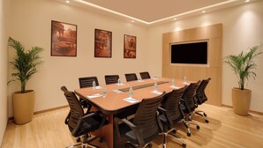 Une salle de conférence avec une longue table, des chaises, un téléviseur à écran plat et des tableaux encadrés accrochés au mur.