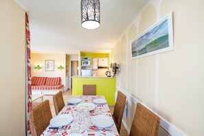Un comedor con una mesa dispuesta para cuatro personas, una cocina al fondo y una sala de estar con un sofá.