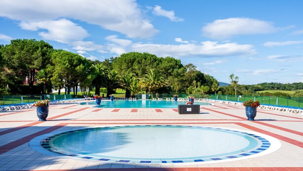 A large outdoor swimming pool with a circular design, surrounded by a tiled deck and potted plants.