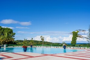 Una piscina con vista al océano, rodeada de vegetación y un cielo despejado.