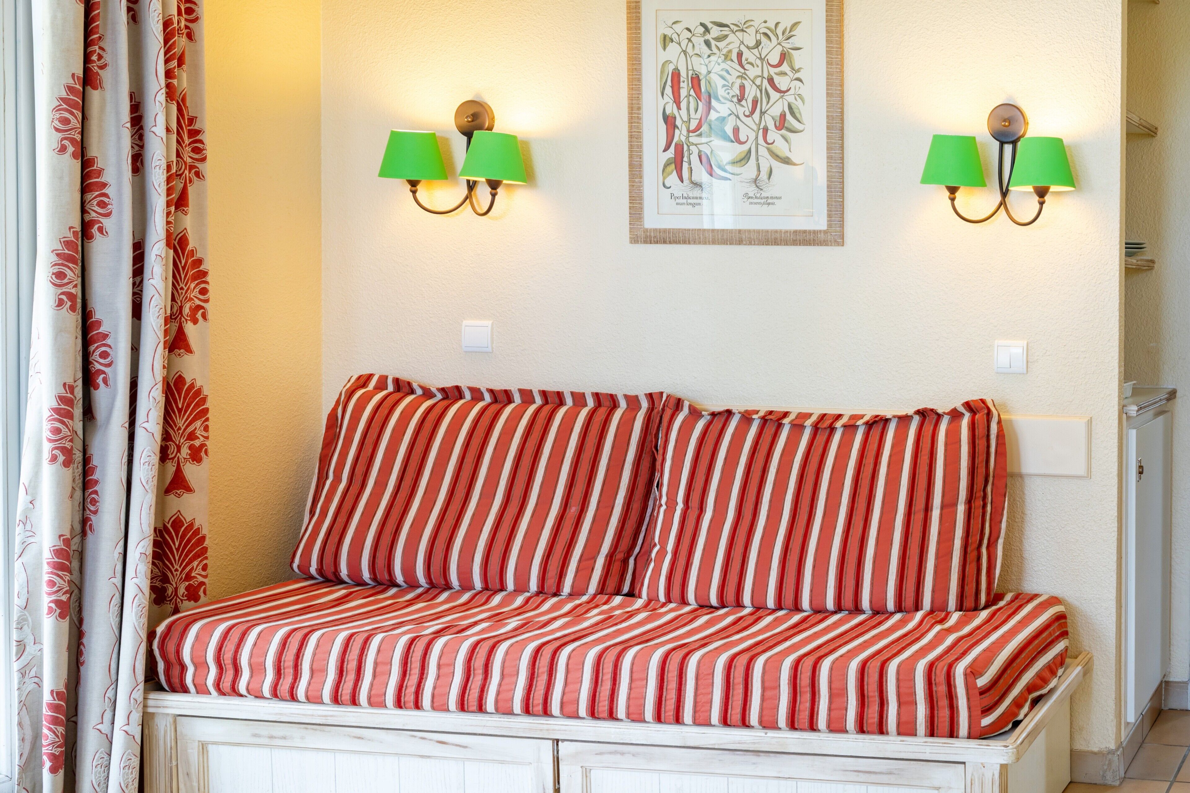 A bed with striped bedding, two wall-mounted lamps, and a framed botanical illustration.