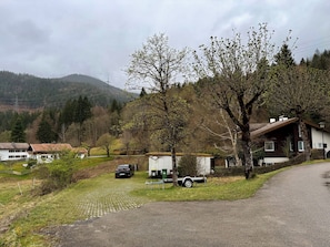 Paisaje rural con casas, una calle pavimentada y un coche estacionado cerca de un edificio.
