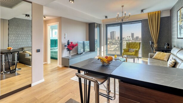 Een moderne keuken met een centraal eiland, een zithoek met een bank en een groot raam met uitzicht op de stad.