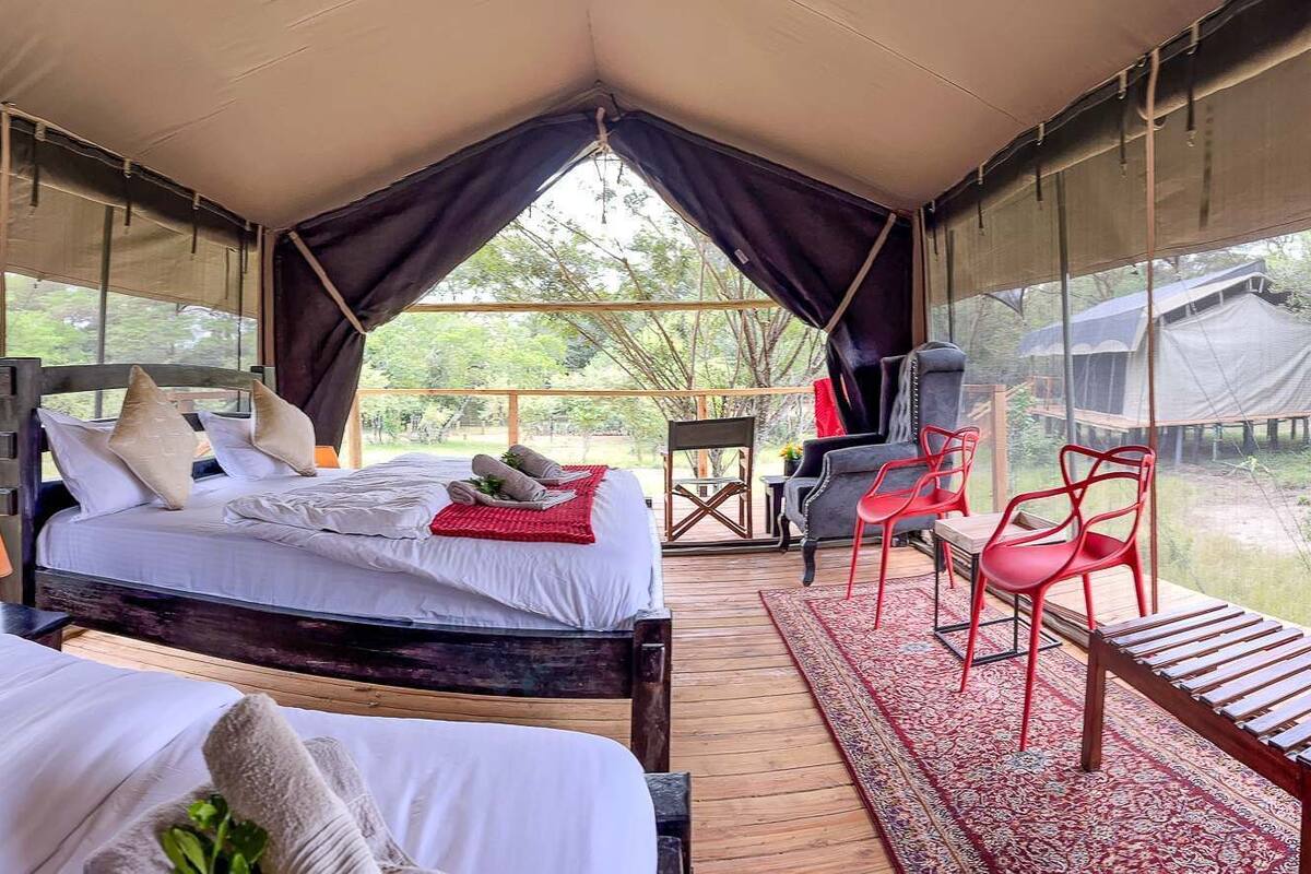 A tented accommodation with two beds, a dining area, and a view of the outdoors.