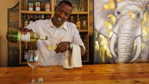 Une personne verse du vin dans un verre au comptoir d’un bar, qui est fait de bois, et on peut voir une peinture d’un éléphant accrochée au mur.
