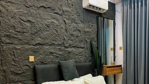Een moderne slaapkamer met een wand met een steenstructuur, een bed met wit beddengoed, een nachtkastje met een lamp en een spiegel boven het bed.