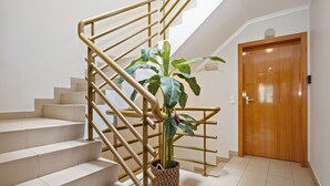 Una escalera con escalones color beige y barandilla dorada, que lleva a una puerta de madera.