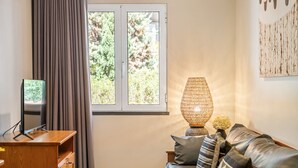 Una sala de estar con un sofá, un televisor, una lámpara y una ventana con cortinas.