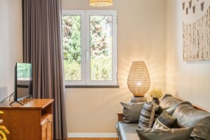 A living room with a sofa, a television, a lamp, and a window with curtains. - Empress 1A by Homie (Funchal)