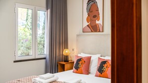 Una habitación de hotel con una cama, almohadas, una mesita de noche, una lámpara y una ventana con cortinas.