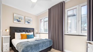 Ein modernes Schlafzimmer mit einem großen Bett, Nachttischen, Kunstwerken an der Wand und Blick durch das Fenster.