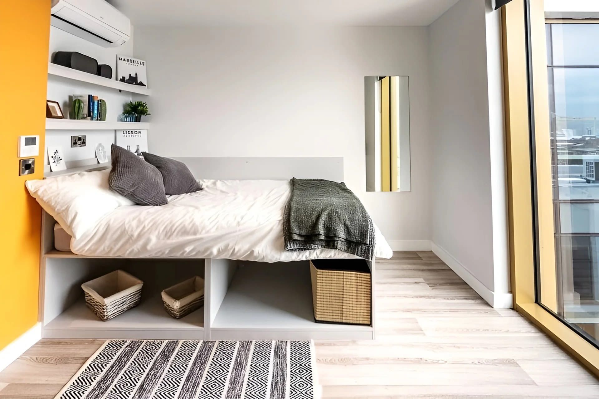 A modern bedroom with a bed, storage shelves, a bedside table, a bedside lamp, and a view through a large window.
