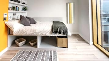 Un dormitorio moderno con cama, estanterías, mesita de noche, lámpara de noche y vistas a través de un ventanal grande.