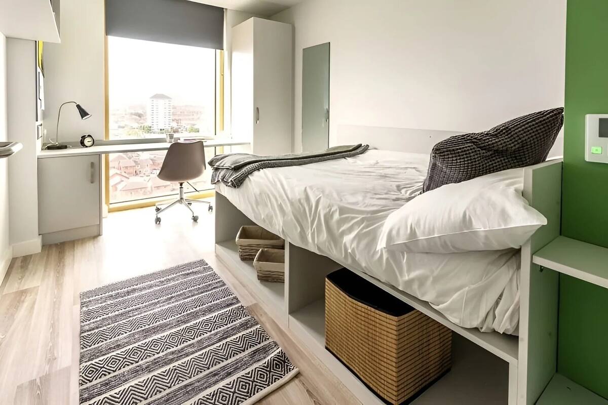 A modern bedroom with a bed, desk, chair, and a view of a cityscape.