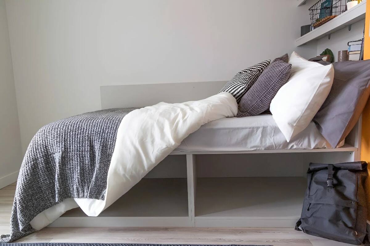 A bed with a white mattress, gray and white bedding, and a gray blanket.