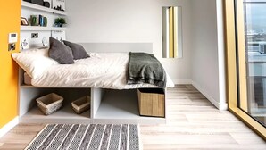 Ein modernes Schlafzimmer mit Bett, Einbauschränken, Nachttisch, Fenster und Blick auf die Stadt.