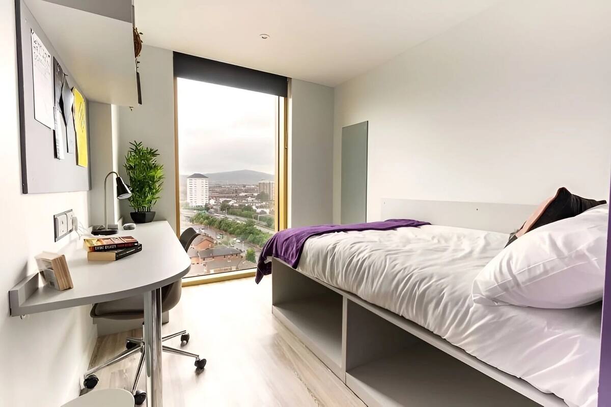 A modern bedroom with a desk, a bed, a large window, and a city view.