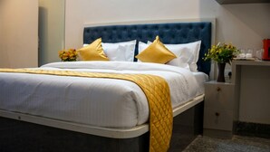 Ein ordentlich gemachtes Bett mit blauem Kopfteil, weißer Bettwäsche und einer gelben Decke.