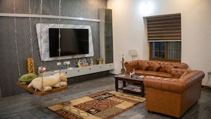 Ein Wohnzimmer mit einer Couch, einem Flachbildfernseher, einem Schrank, einer Lampe und einem gemusterten Teppich.