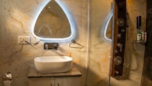 Ein Badezimmer mit Marmorwaschtisch, einem großen, ovalen Spiegel, einer integrierten Dusche und einem Handtuchhalter.