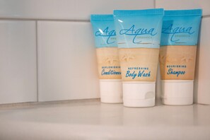 Travel-sized Aqua Organics toiletries set against white subway tile. - | The Funky Mermaid at East Bay Inn Pet Friendly (Panama City)